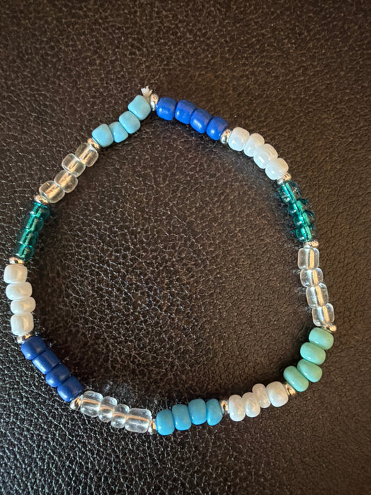 Beaded bracelet with blue, white, and green beads on a dark textured surface