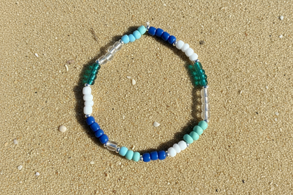 Beaded bracelet with multiple blue and white beads on sandy beach background 