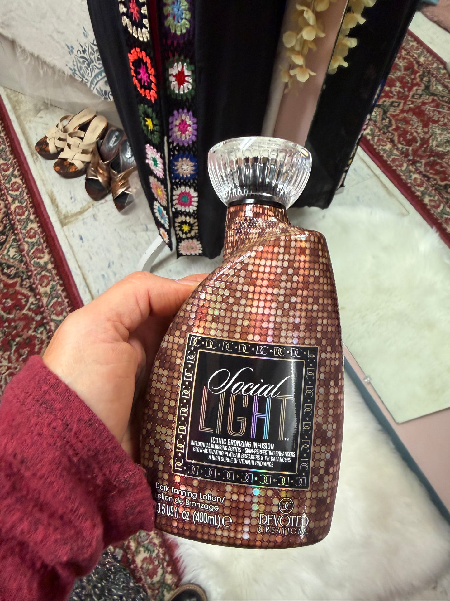 Hand holding a bottle of tanning lotion labeled 'Social Light' with a colorful background
