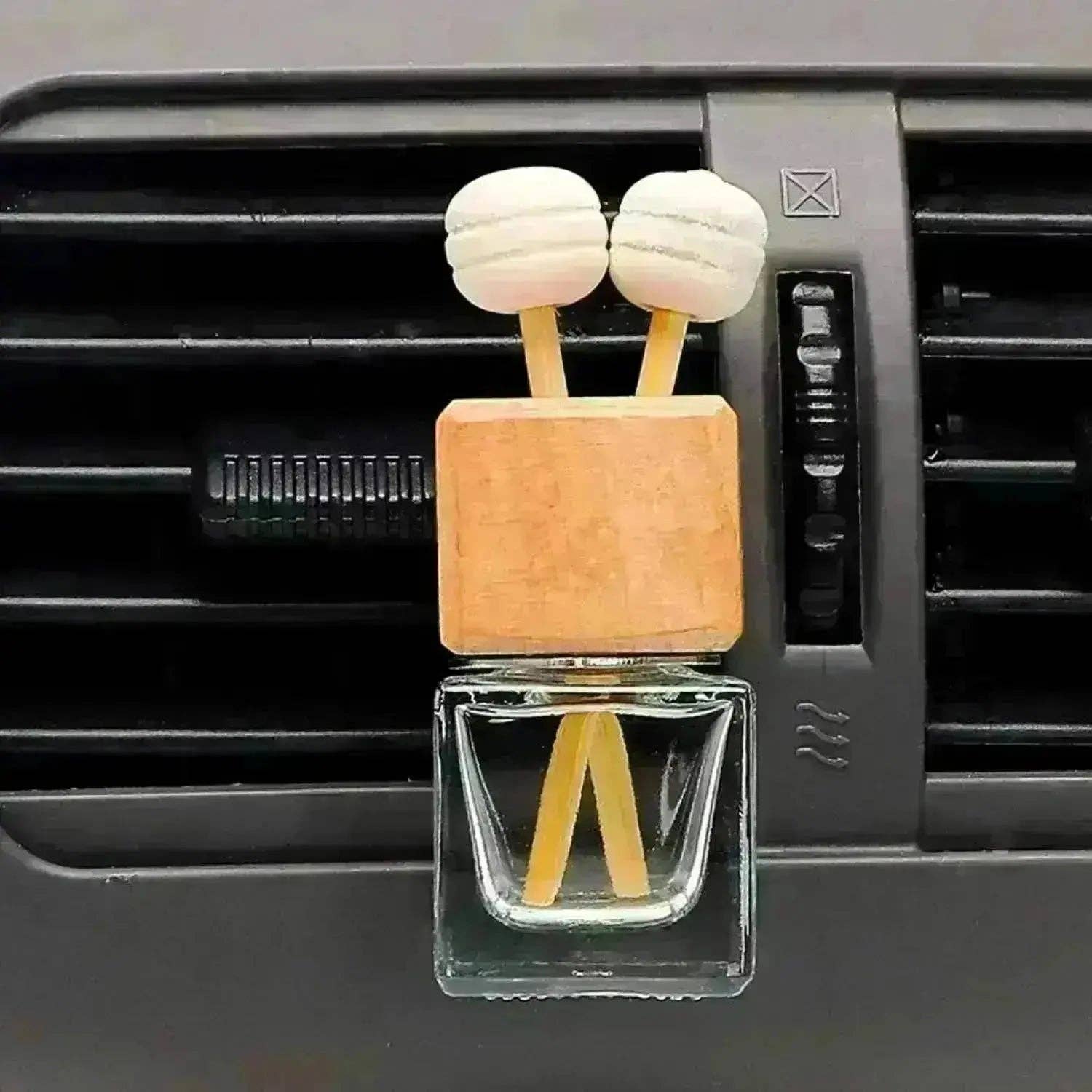 Car air freshener shaped like a robot with a wooden top and glass body, attached to a car's air vent.