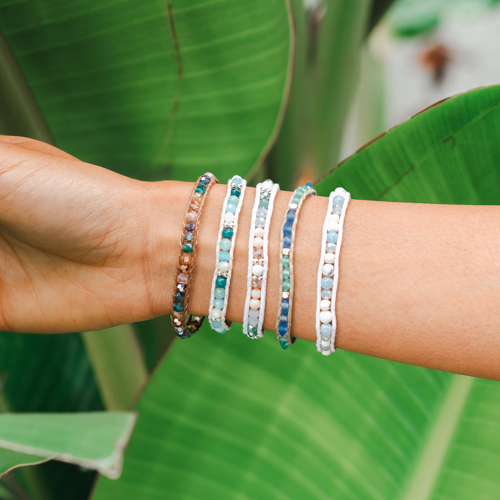 Wrist with multiple beaded bracelets against a green leaf background