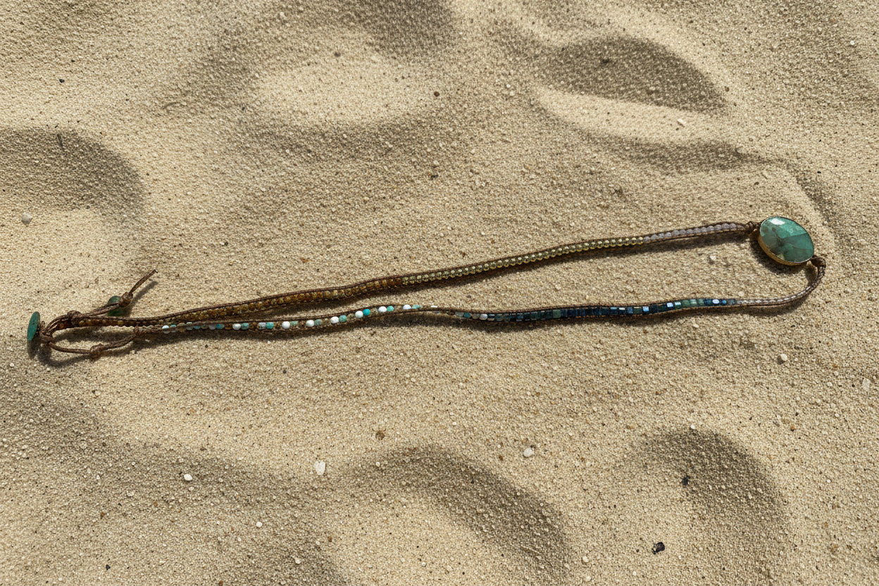 A multi stlarge oval green wrap bracelet, laid out on a sand background