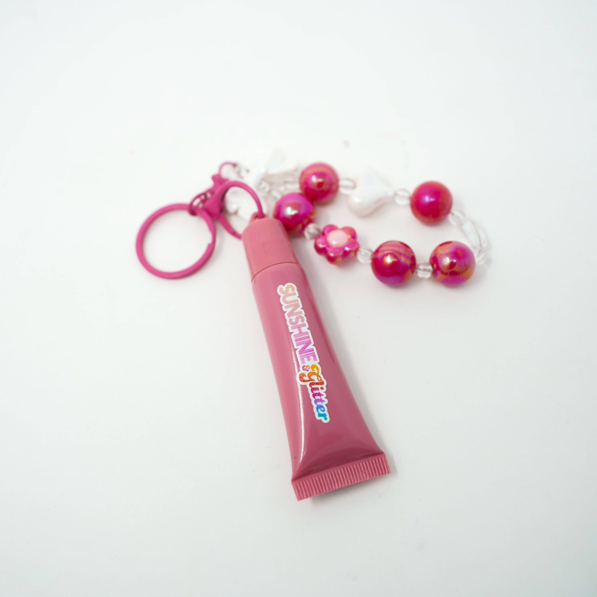Pink lip gloss with a keychain and beads on a white background