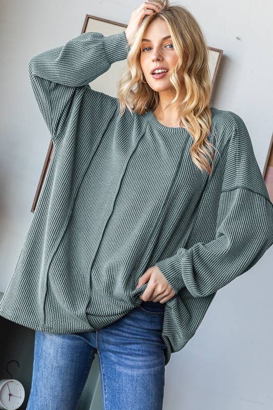 Woman wearing a green oversized sweater and blue jeans against a white wall.