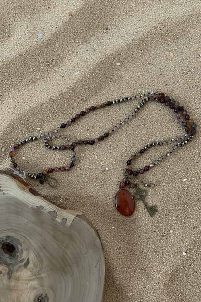 A beaded necklace with a dark brown oval pendant and a vintage-style metal key charm.
