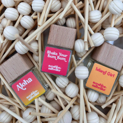 Three small wooden boxes with colorful labels on a bed of wooden sticks and white beads.