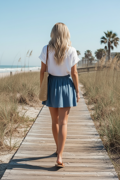 back view of woman walking on a boardwalk wearing a white shirt and flowy blue shorts with pockets