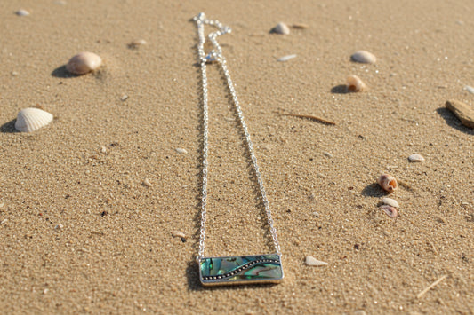 Necklace with a rectangular abalone pendant on a sandy background