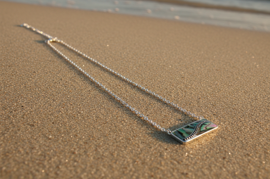Necklace with a abalone wavependant on sand near water