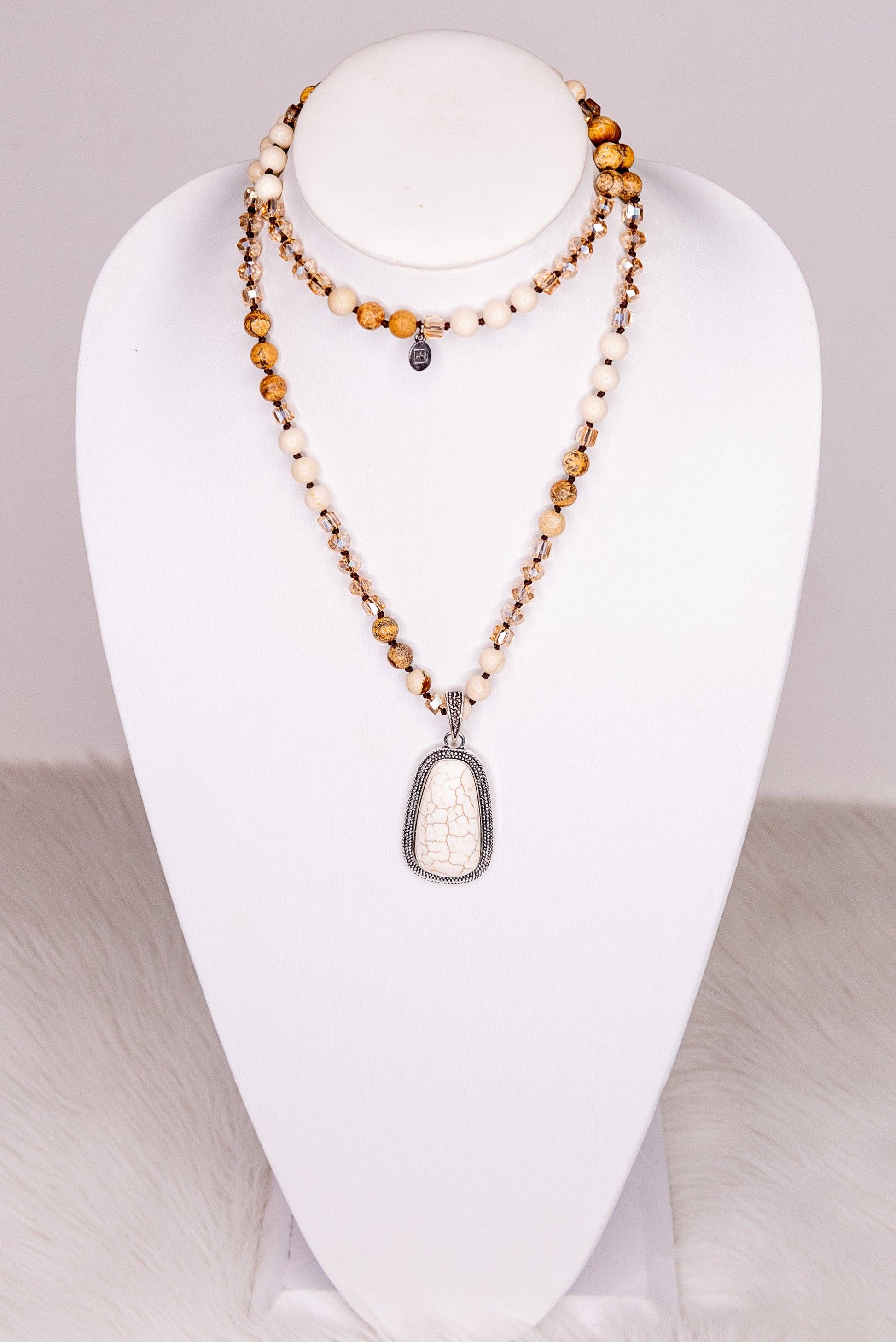 Necklace with a large white pendant on a white mannequin bust against a neutral background