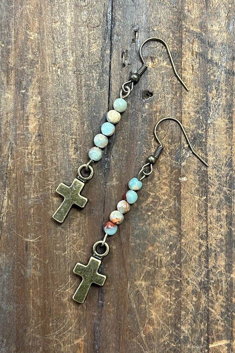 Pair of earrings with cross charms and beaded extensions on a wooden surface