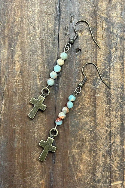 Pair of earrings with cross charms and beaded extensions on a wooden surface