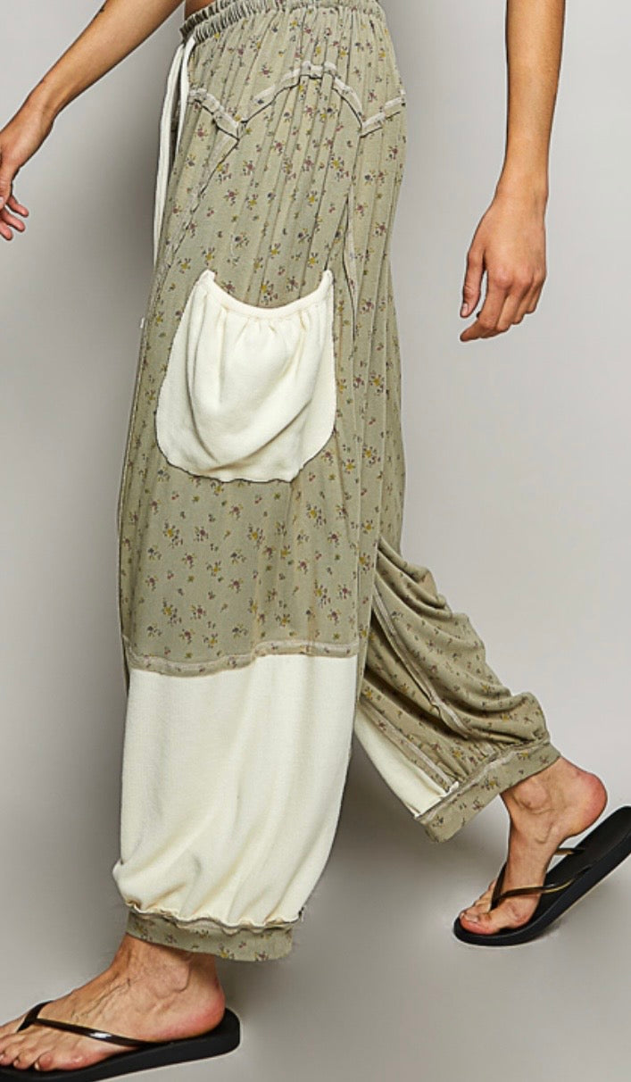 Woman wearing flowing sage colored ditzy flower print pants with cream patch pockets Side view