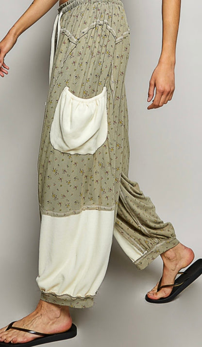 Woman wearing flowing sage colored ditzy flower print pants with cream patch pockets Side view