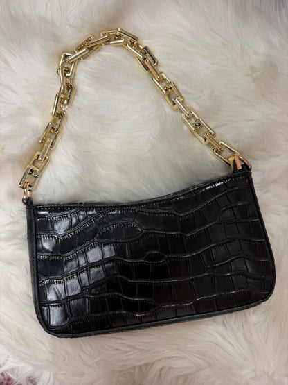 A black crocodile-embossed shoulder bag with a chunky gold chain strap, displayed on a white faux fur background.