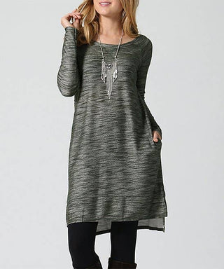 Woman wearing a long, dark gray tunic with a plain background