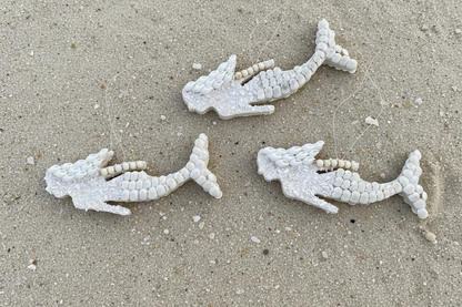 Three white mermaid orna on a sandy surface