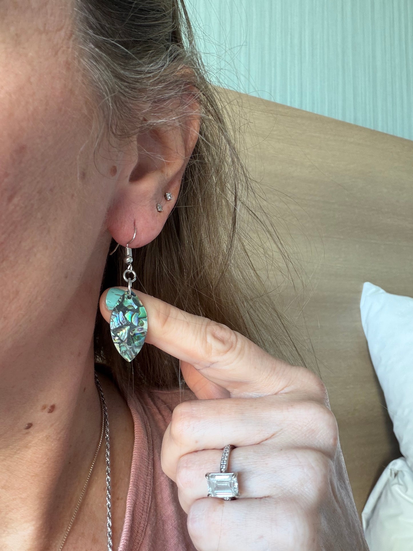 Close-up of a person wearing an abalone surfboard shaped earring