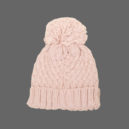 Pink knitted beanie with a pom-pom on a beige background