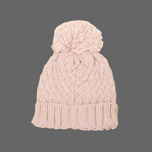 Pink knitted beanie with a pom-pom on a beige background