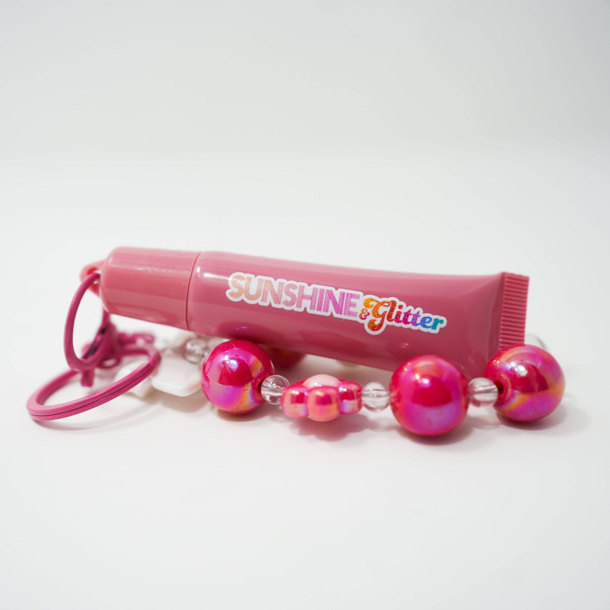 Pink lip gloss with beads on a white background