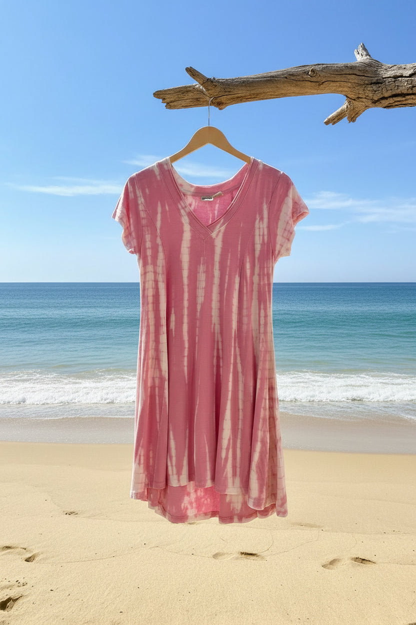 Pink tie dye v-neck dress hanging from a branch on a beachy shoreline