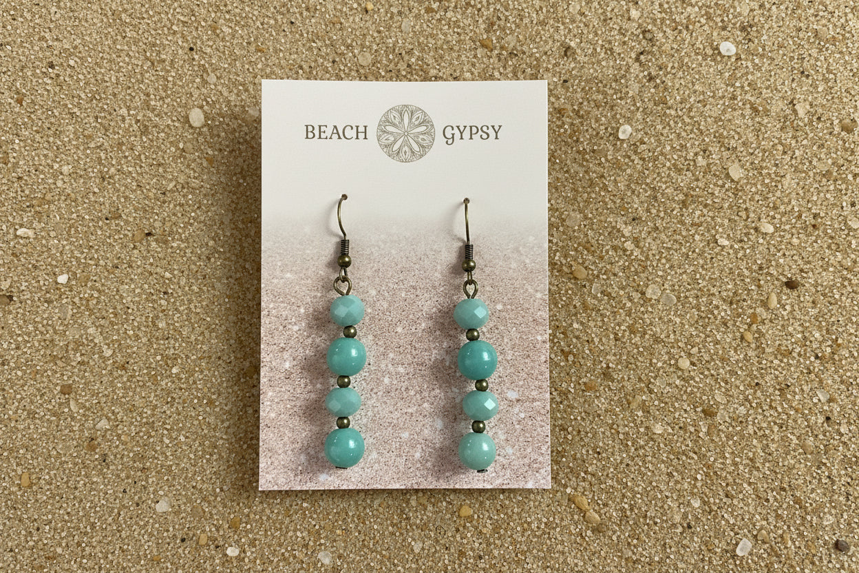 Turquoise beaded earrings on a 'Beach Gypsy' branded card against a sand background