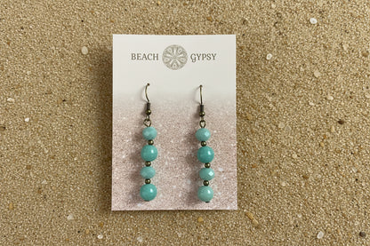 Turquoise beaded earrings on a 'Beach Gypsy' branded card against a sand background