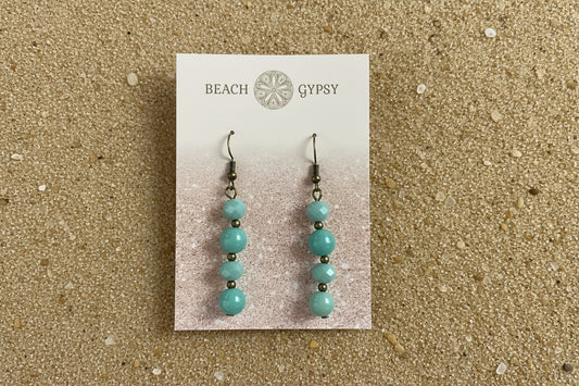Turquoise beaded earrings on a 'Beach Gypsy' branded card against a sand background