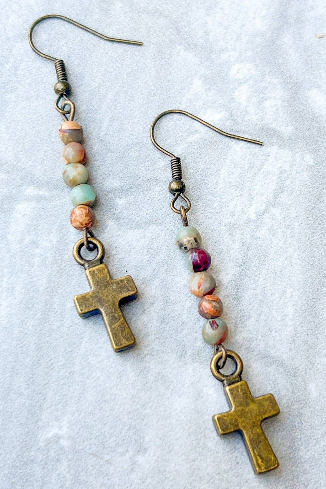 Pair of earrings with cross charms and multicolored beads on a light background