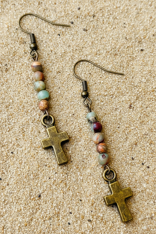 Pair of earrings with cross charms and multicolored beads on a sand background