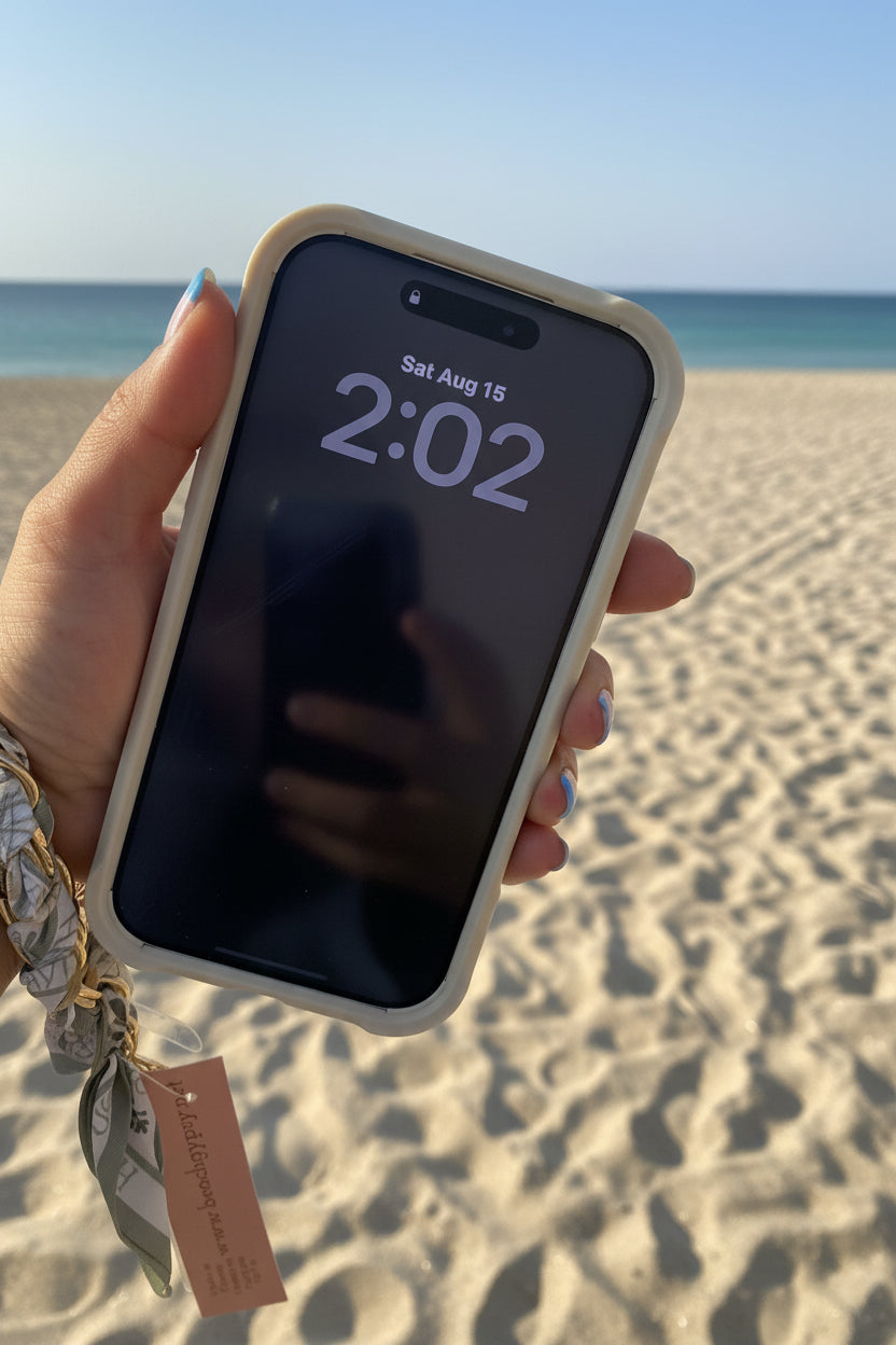 Hand holding a cell phone with a scarf cell phone holder on a beach background 
