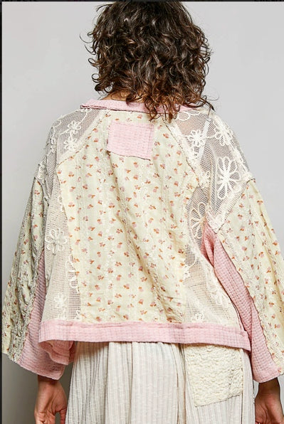 A person shown from the back wearing a patchwork-style top with floral and lace panels in cream, pink, and beige tones, paired with light striped pants against a plain light gray background.