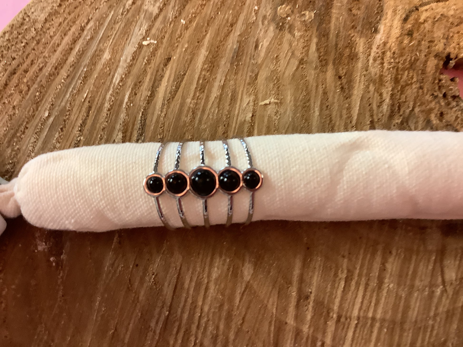 Five silver rings with black round stones in rose gold bezels, displayed on a white fabric ring holder over a wooden surface.