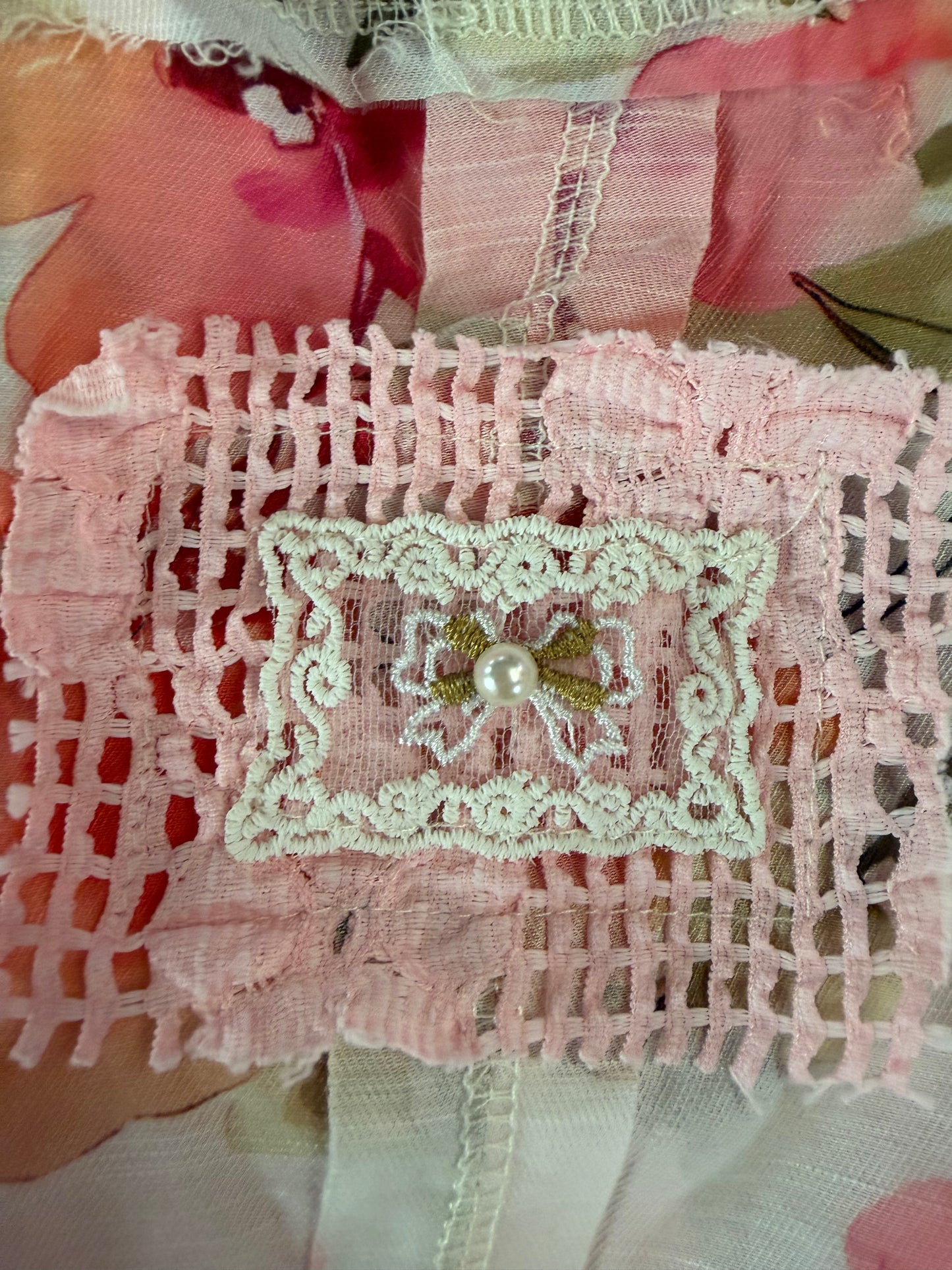 Pink lace fabric with a decorative patch featuring a pearl and green leaves.