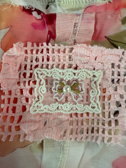Pink lace fabric with a decorative patch featuring a pearl and green leaves.