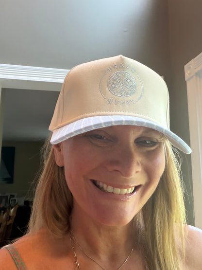 A woman wearing a beige trucker-style cap with a white brim and a Beach Gypsy embroidered logo on the front, photographed indoors.