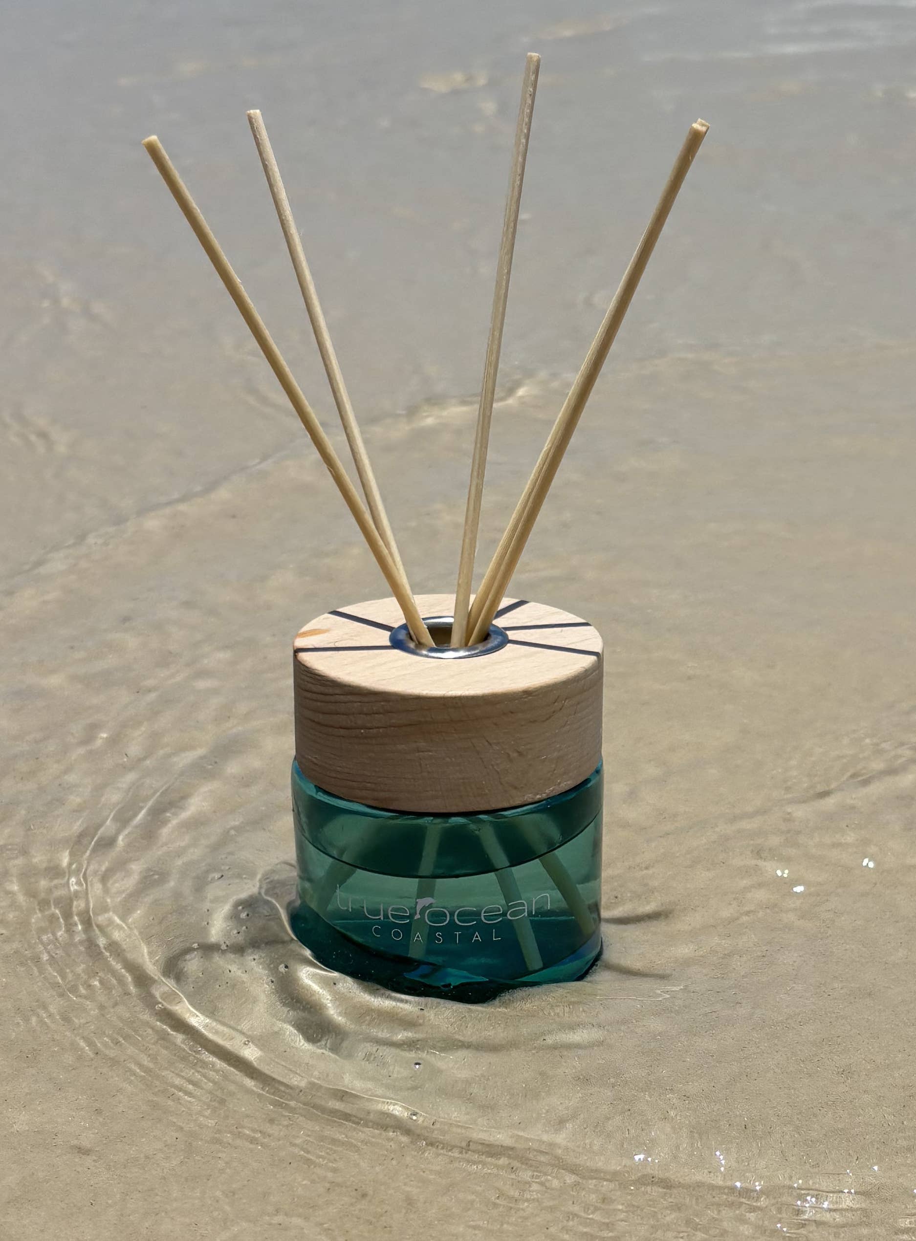 Reed diffuser with wooden top and green base on wet sand