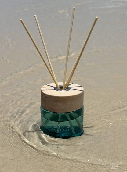 Reed diffuser with wooden top and green base on wet sand
