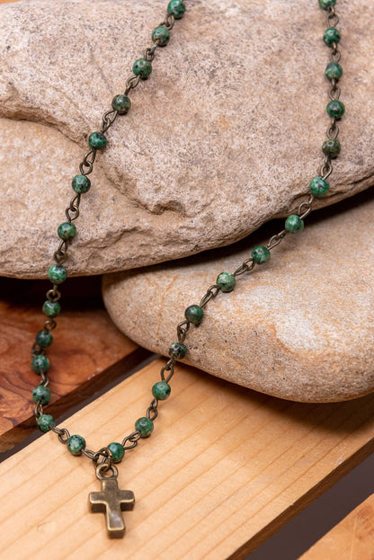 Green beaded necklace with a cross pendant on a stone surface