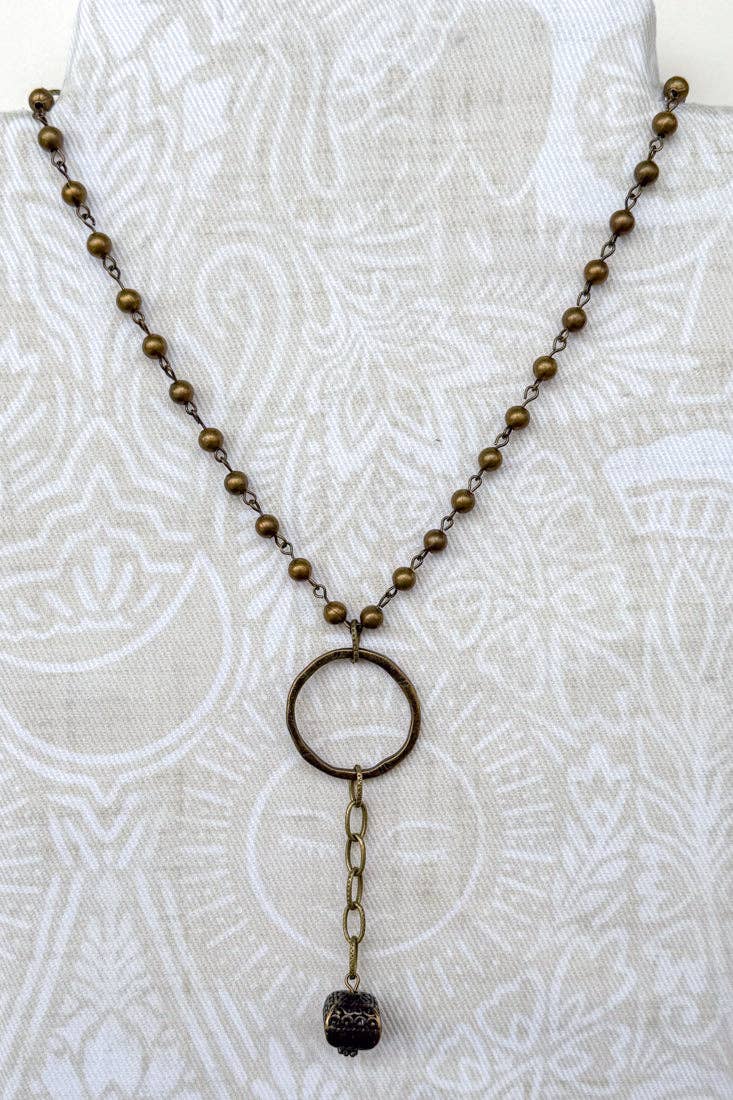 Bronze beaded necklace with a circular pendant on a white textured background