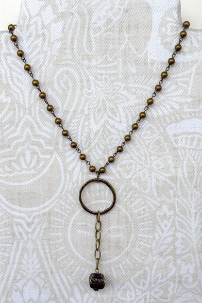 Bronze beaded necklace with a circular pendant on a white textured background