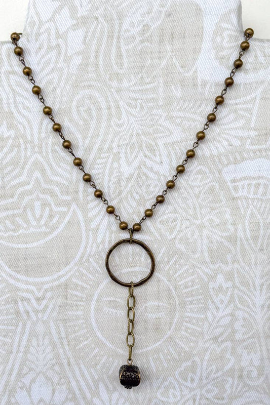 Bronze beaded necklace with a circular pendant on a white textured background