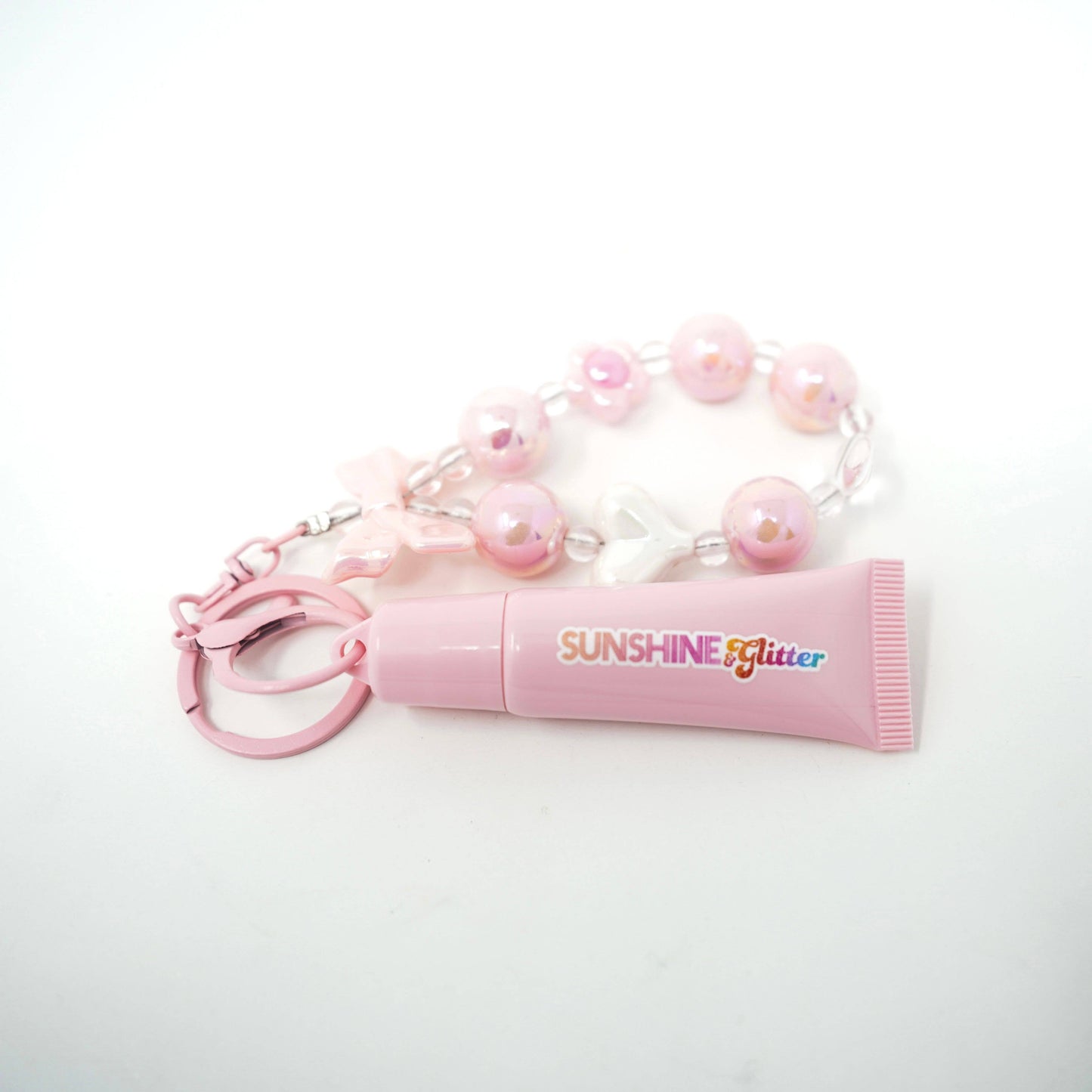 Pink lip balm with 'Sunshine Glitter' text and a beaded keychain on a white background