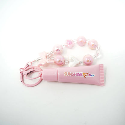 Pink lip balm with 'Sunshine Glitter' text and a beaded keychain on a white background