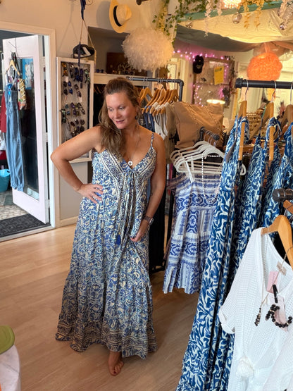 Woman in a blue Contessa open back dress standing in a clothing store with racks of clothes.