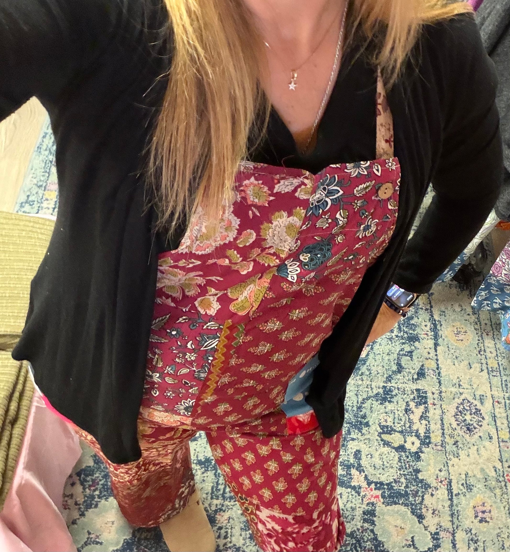 Person wearing a black top and red floral jumpsuit standing on a patterned carpet in a boutique 