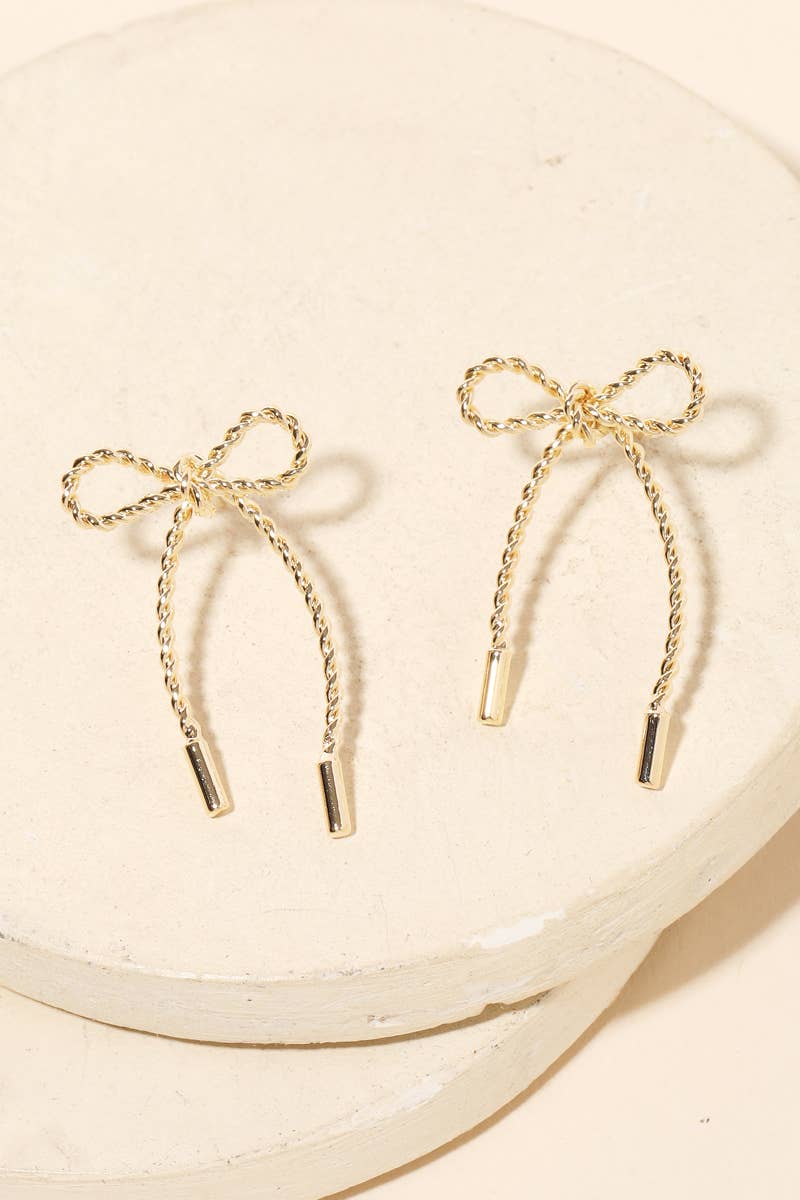 Gold bow-shaped earrings on a beige plate