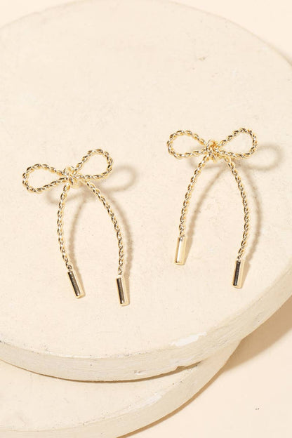 Gold bow-shaped earrings on a beige plate