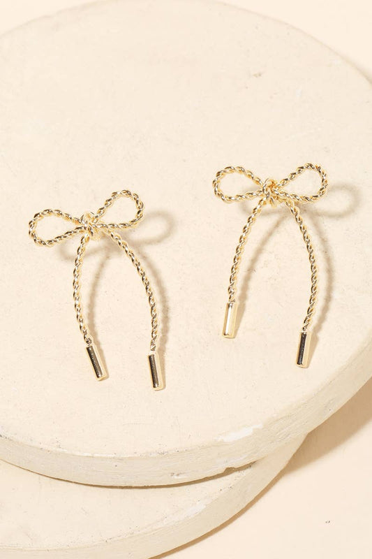 Gold bow-shaped earrings on a beige plate